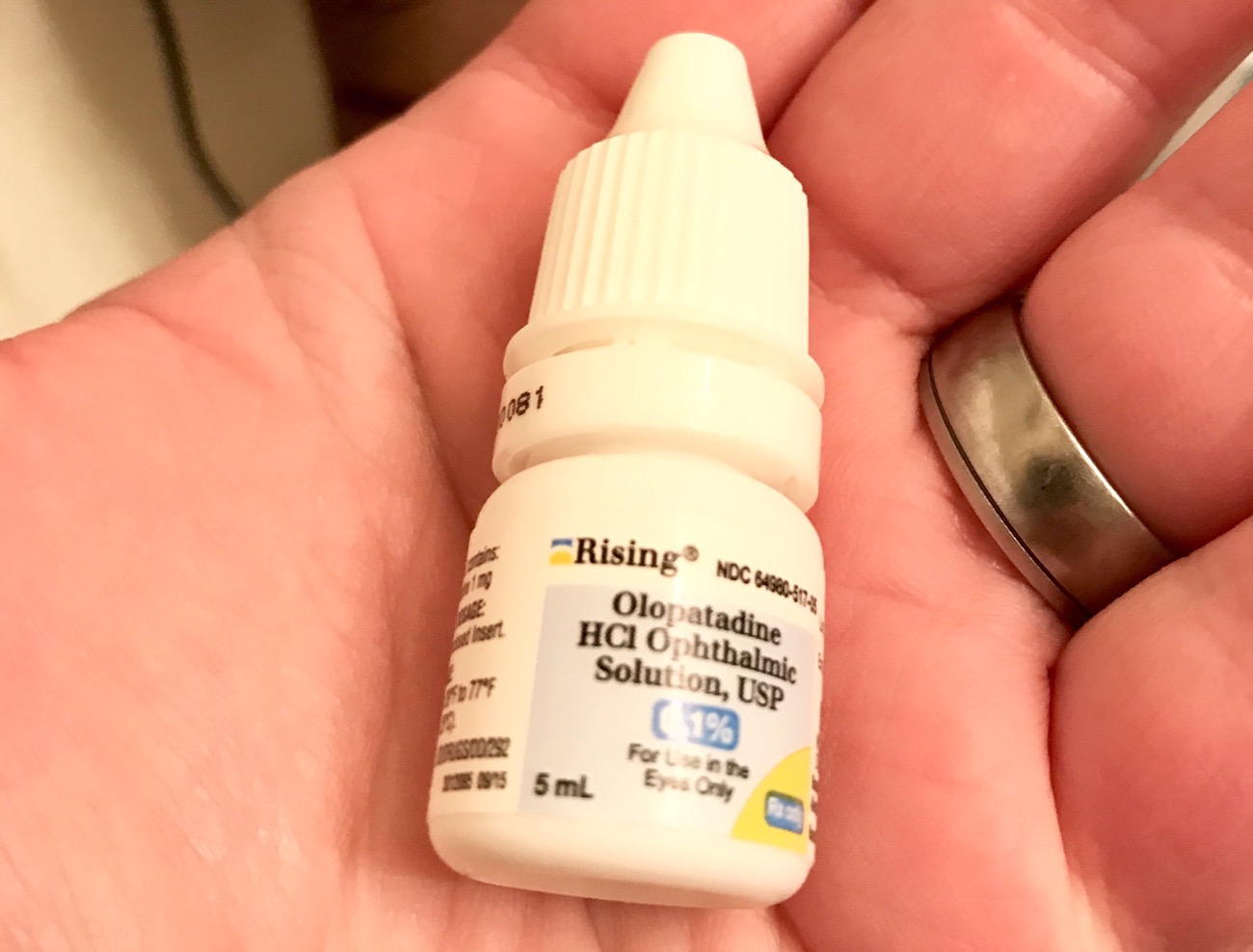A hand holding a 5ml bottle of olopatadine eye drops